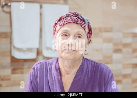 Ältere Frau, die sich um ihr Gesicht kümmert. Alte Frau, die sich im Spiegel ansieht Stockfoto