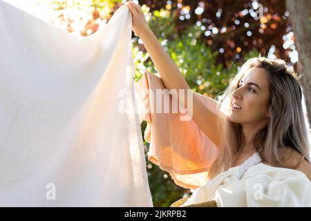 Porträt einer jungen schönen Frau, die im Sommer im Garten im Freien mit Hintergrundbeleuchtung Wäsche macht Stockfoto