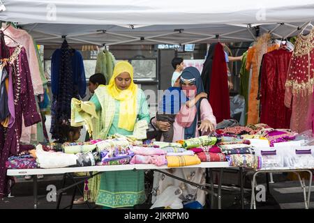 Auf einer Bangladeshi Street Fair auf der Church Avenue im Stadtteil Kensington in Brooklyn, New York, verkaufen Frauen bunte Kleider und Material. Stockfoto