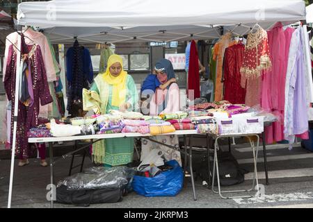 Auf einer Bangladeshi Street Fair auf der Church Avenue im Stadtteil Kensington in Brooklyn, New York, verkaufen Frauen bunte Kleider und Material. Stockfoto