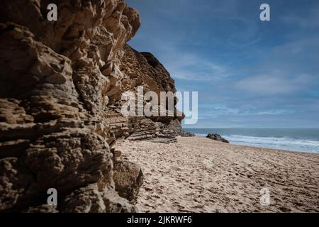 Praia da Murtinheira in Quiaios, Portugal, ein ruhiger und wilder Strand abseits der Menschenmassen. Nahaufnahme von felsigen Küsten, Sand und blauem Himmel. Foto im Landscape-Bild Stockfoto