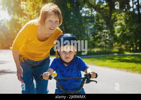 Großmutter lehrt seinen Enkel Fahrrad zu fahren. Kind lernt Fahrrad zu fahren Stockfoto