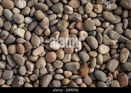 Abstrakter Hintergrund aus runden natürlichen unregelmäßigen rauen braunen und beigen Kieselsteinen. Stockfoto