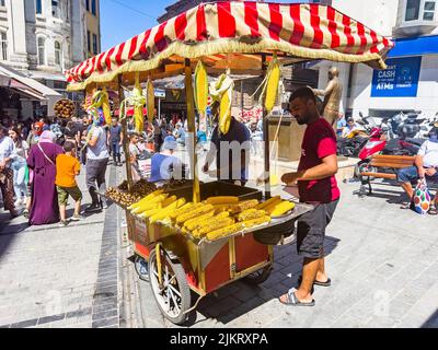 Istanbul, Türkei, 07.14.2022: Mann, der gegrillten Mais verkauft. Street Verkäufer von Fast Food mit gekochtem, gegrilltem Mais und Kastanien auf traditionellen türkischen Karren Stockfoto