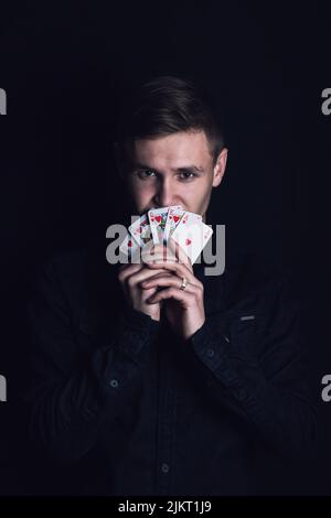 Erfolgreicher Pokerspieler hält eine gewinnende Royal Flush Kombination. Glücklicher Spieler mit Spielkarten auf dunklem Hintergrund. Gewinner des Casino-Turniers, V Stockfoto