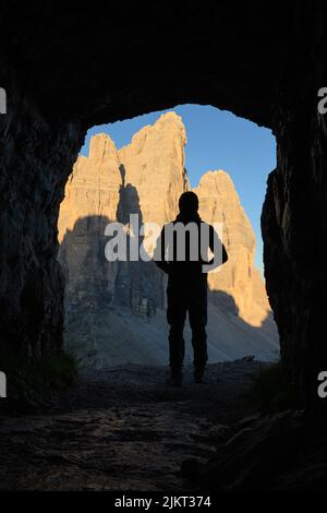 Silhouette eines Touristen, der den Blick auf die drei Zinnen von Lavaredo genießt, umrahmt von einer Höhle. Stockfoto