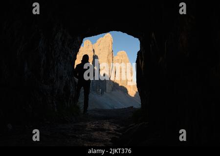 Silhouette eines Touristen, der den Blick auf die drei Zinnen von Lavaredo genießt, umrahmt von einer Höhle. Stockfoto