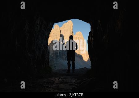 Silhouette eines Touristen, der den Blick auf die drei Zinnen von Lavaredo genießt, umrahmt von einer Höhle. Stockfoto