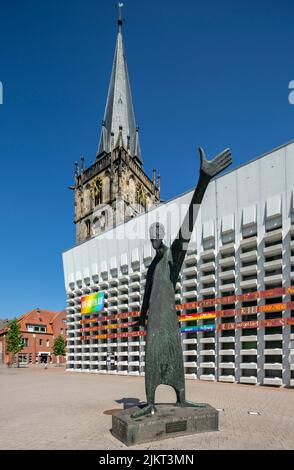 Deutschland, Ahaus, Westmuensterland, Münsterland, Westfalen, Nordrhein-Westfalen, NRW, Katholische Mariä Himmelfahrt-Kirche auf dem Marktplatz stammt der Kirchturm aus der historischen Kirche und das Kirchenschiff wurde von Erwin Schiffer als Betonbau befestigt, vor der Skulptur 'der Mahner' von Hilde Schuerk frisch Stockfoto