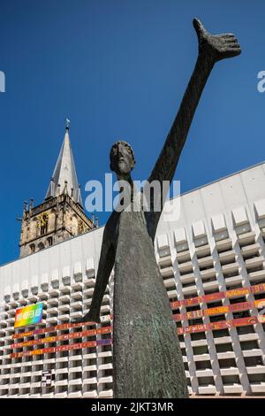 Deutschland, Ahaus, Westmuensterland, Münsterland, Westfalen, Nordrhein-Westfalen, NRW, Katholische Mariä Himmelfahrt-Kirche auf dem Marktplatz stammt der Kirchturm aus der historischen Kirche und das Kirchenschiff wurde von Erwin Schiffer als Betonbau befestigt, vor der Skulptur 'der Mahner' von Hilde Schuerk frisch Stockfoto