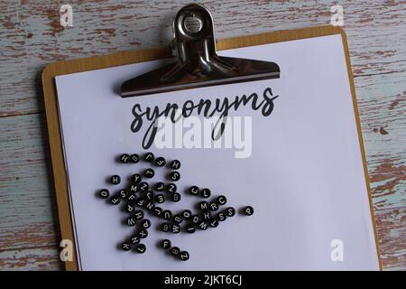 Bild von oben der Zwischenablage aus Papier mit Synonymen und Alphabetischen Perlen. Stockfoto
