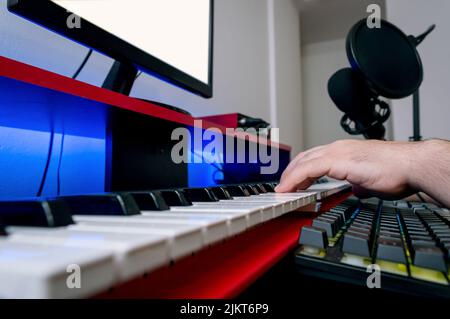 Nahaufnahme der männlichen kaukasischen Hände, die im heimischen Aufnahmestudio E-Piano spielen und Musik produzieren und komponieren. Stockfoto