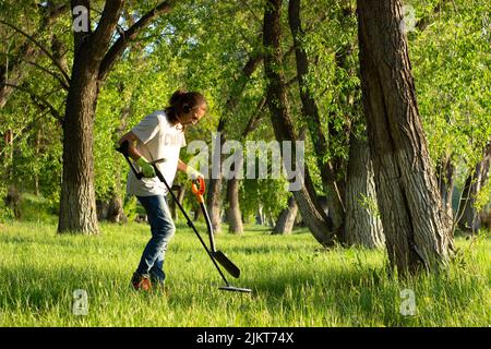 Ein Mann in Handschuhen sucht mit Hilfe eines Nadelpointers im Frühlingswald nach einem Schatz im Boden. Schaufel davor Stockfoto