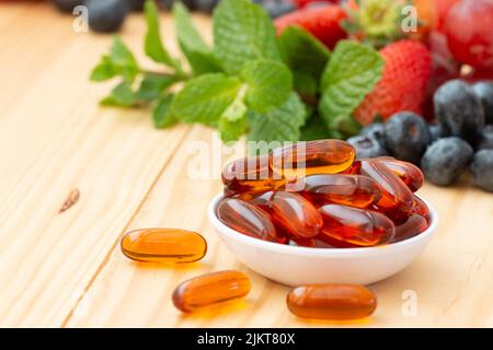 Lecithin Gel Vitamin-Supplement-Kapseln in einer kleinen Tasse auf dem Holztisch mit Varietät Obst. Stockfoto