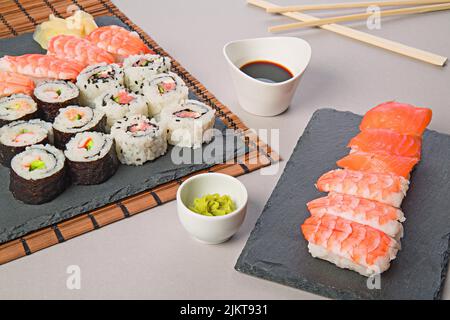 Eine Nahaufnahme eines Lachs-Sushi-Sets und Makizushi mit einer weißen Schüssel Sojasauce auf dem Tisch Stockfoto
