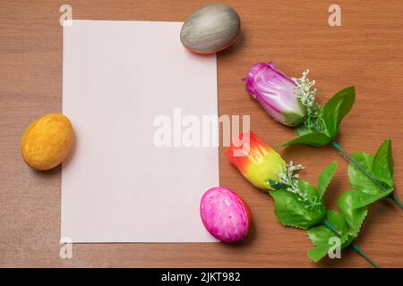 Eine Nahaufnahme von Ostereiern und künstlichen Blumen auf einer Holzfläche mit weißem Textraum Stockfoto