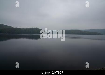 Eine schöne Aussicht auf einige kleine Hügel mit Bäumen, die sich im See bei nebligen Wetter spiegeln. Stockfoto