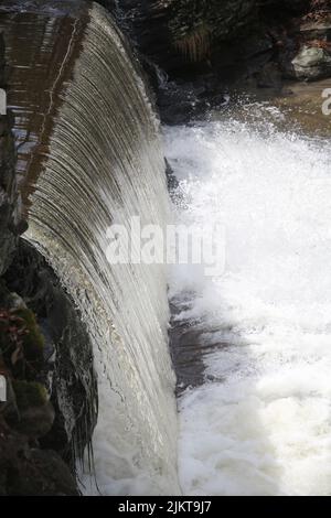 Ein Schuss des starken Flusses eines Wassers, das zu einem Fluss hinunterfließt Stockfoto