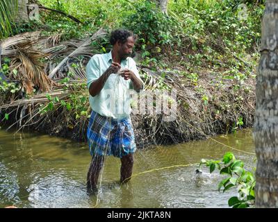 Das Foto zeigt einen indischen Fischer in New Mangalore, der das traditionelle Fischen mit einem Netz macht. Stockfoto