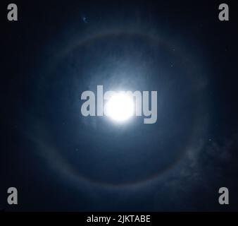 Eine wunderschöne Aufnahme des Mondes, der in den Himmel scheint, mit einem Halo-Kreis in der Nacht Stockfoto