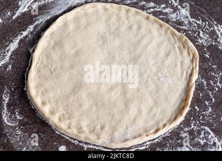 Pizzateig auf bemehlten Schieferoberfläche ausgerollt, overhead mit Tageslicht fotografiert Stockfoto