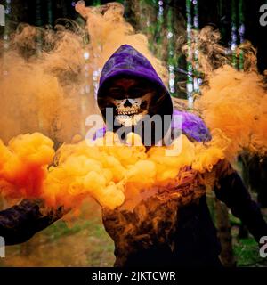 Eine Person in einer Totenkopfmaske, die an Halloween um einen bunten Rauch herumläuft Stockfoto