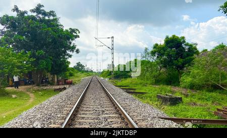 Eine Nahaufnahme von Kieselsteinen auf der Eisenbahn, umgeben von viel Grün an einem bewölkten Tag Stockfoto