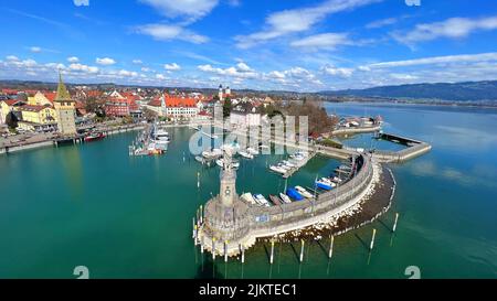 Eine Luftaufnahme des Hafens von Lindau mit einer historischen Brücke und der Statue mit dem Stadtbild von Lindau im Hintergrund Stockfoto