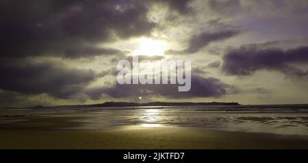 Die Sonne scheint hinter dunklen Wolken über dem Ufer Stockfoto