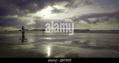 Die Sonne scheint hinter dunklen Wolken über den Surfern am Strand Stockfoto