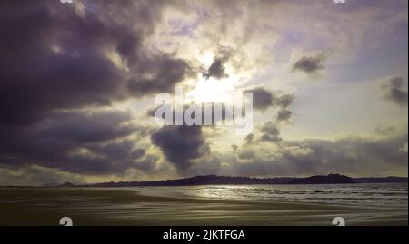 Die Sonne scheint hinter dunklen Wolken über dem Ufer Stockfoto