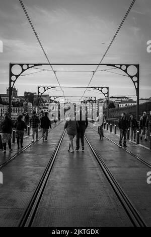 Eine vertikale Graustufenaufnahme von Wanderern auf der Ponte D Luis Brücke in Porto, Portugal Stockfoto