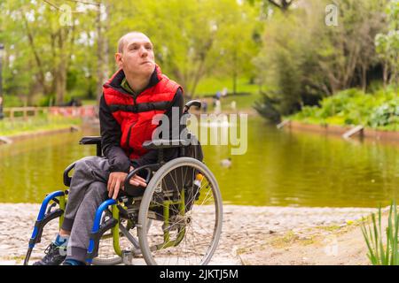 Porträt eines gelähmten jungen Mannes in einem öffentlichen Park in der Stadt. Nachdenklich im Rollstuhl sitzen Stockfoto