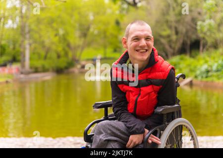 Ein gelähmter junger Mann in einem öffentlichen Park in der Stadt. Sitzen im Rollstuhl Stockfoto