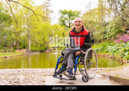 Porträt eines gelähmten jungen Mannes in einem öffentlichen Park in der Stadt. Sitzen im Rollstuhl Stockfoto