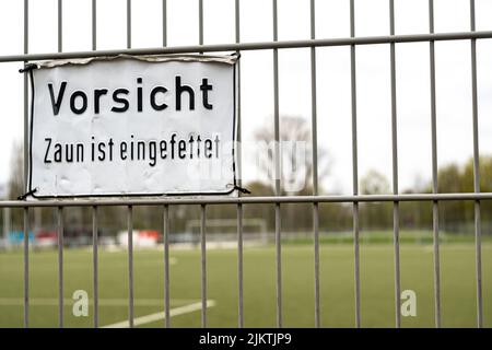 Ein Schild mit der Aufschrift „Achtung, der Zaun ist geölt“ auf einem weißen Plakat, das auf Deutsch an einem Zaun angebracht ist Stockfoto