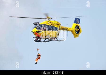 Eine Person rappelt bei einem Flugschuss von einem schwebenden ADAC-Rettungshubschrauber ab. Deutsche Luftambulanz, Such- und Rettungsinfrastruktur. Stockfoto