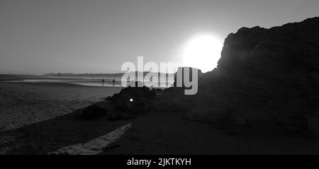 Eine Graustufe von Meer oder Ozeanküste mit Sonne, die ringsum leuchtet und massiven Felsen im Vordergrund Stockfoto