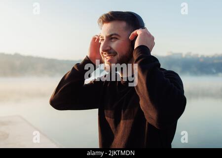 Mann, der draußen Musik hört. Fröhlicher, gutaussehender Mensch, der Kopfhörer hört. Stockfoto