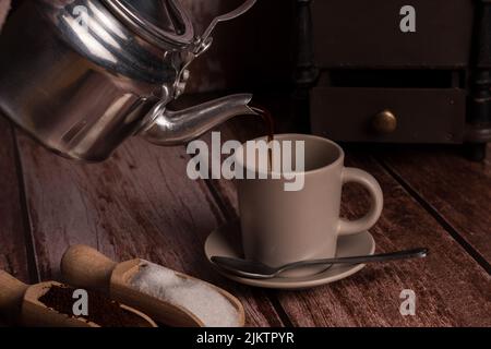 Metallvase gießt Kaffee in eine Keramikschale auf einem Holztisch Stockfoto