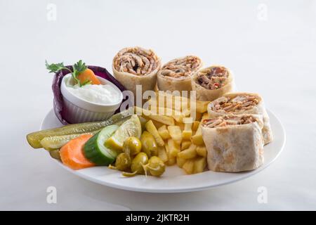 Das Huhn wickelt sich mit Pommes frites, Gurken, Gemüse und einer Sauce auf einen weißen Teller Stockfoto