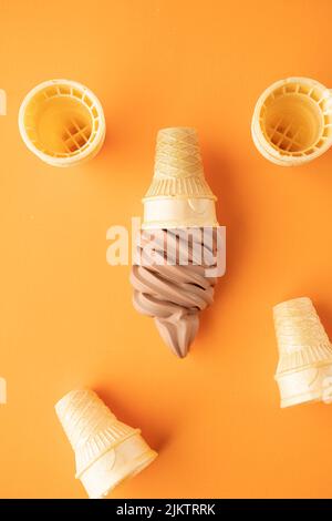 Eine Ansicht von oben auf Schokoladeneis und vier Waffelkegel um ihn herum auf einer orangefarbenen Oberfläche, die lecker aussieht Stockfoto