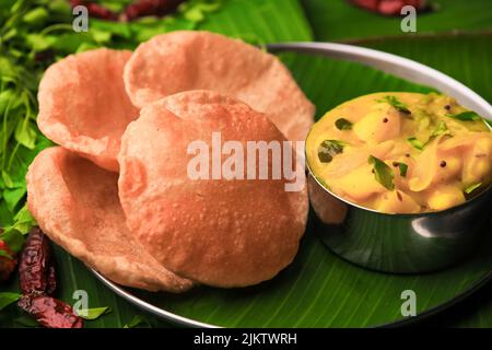 südindische berühmte Frühstückspoori oder puri mit Kartoffelpuffer, serviert auf einem Teller mit Bananenblatt-Nahaufnahme mit selektivem Fokus und Unschärfe Stockfoto