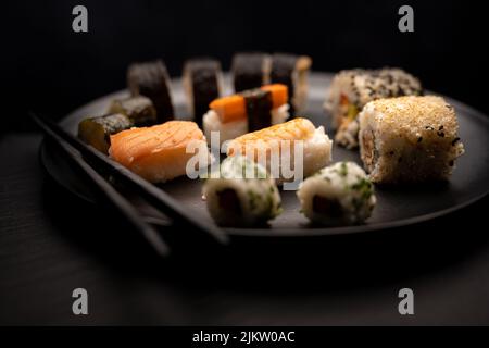 Sushi auf schwarzem Teller mit schwarzen Essstäbchen dunklem Hintergrund Stockfoto