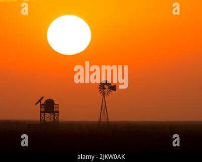 Eine schöne Aufnahme eines Wasserturms und einer Windpumpe während des Sonnenuntergangs Stockfoto