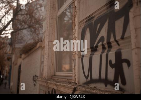 Ein schwarzes Graffiti auf einer beigefarbenen Betonwand am Fenster Stockfoto