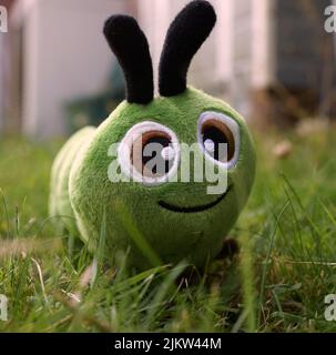 Lustige grüne Plüsch Raupe im Gras. Der Hintergrund ist unscharf. Ein Spielzeug für Kinder oder Babys. Stockfoto