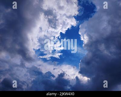 Licht, das zwischen dunklen Wolken gegen einen sehr blauen Himmel scheint. Abstraktion. Stockfoto