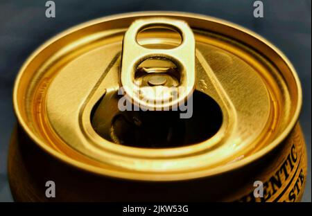 Die offene Spitze eines goldenen Bieres kann in einem 35-Grad-Winkel auf grauem Hintergrund betrachtet werden. Stockfoto