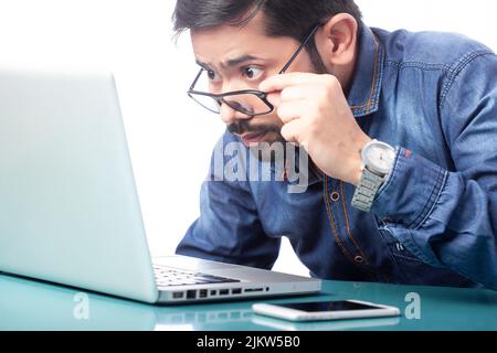 Staunender Mann, der auf den Laptop-Bildschirm über einer Brille auf weißem Hintergrund blickt Stockfoto
